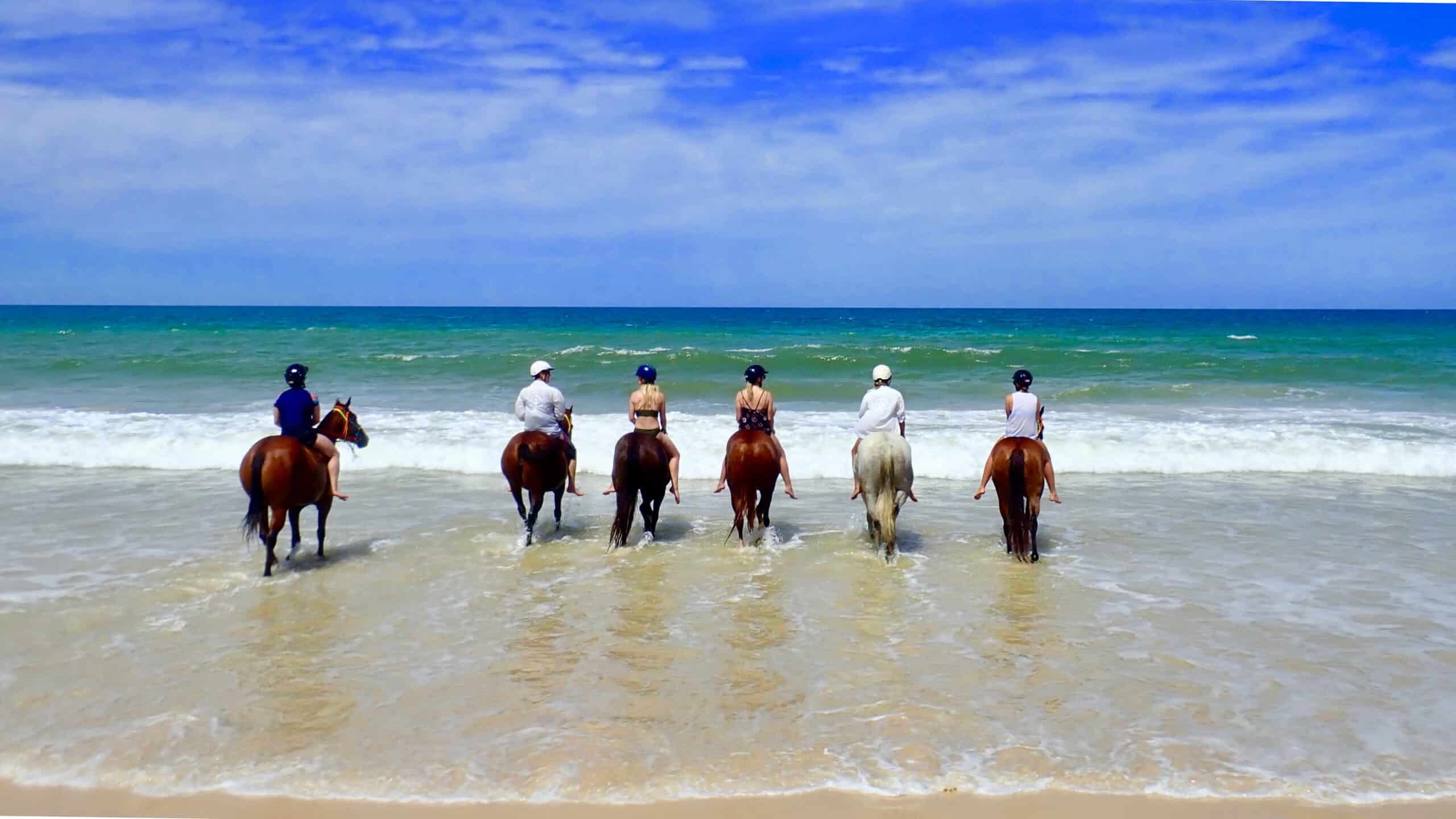 Six people riding horses in the ocean at Rainbow Beach Holiday Village